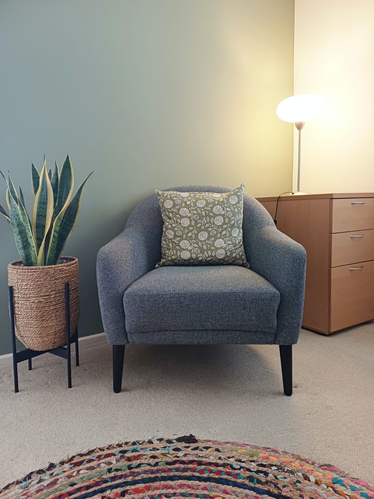 A comfortable armchair in the counselling room beside a plant and warm lamp